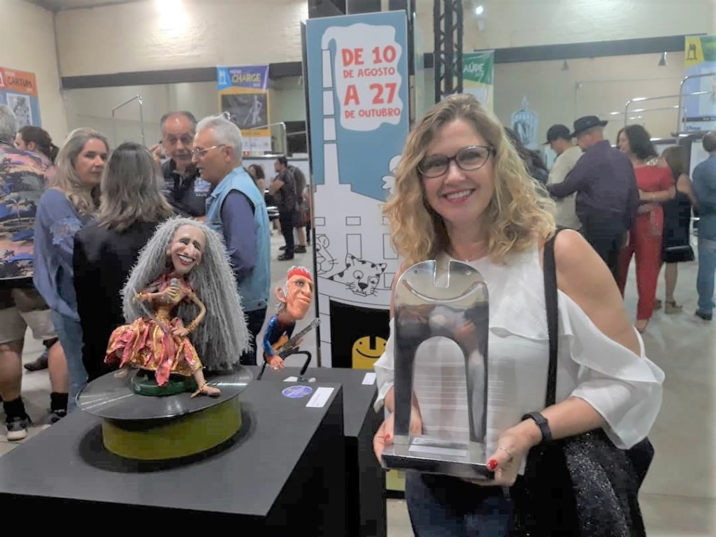 Synnöve Hilkner, cartunista da ASN, o troféu do Prêmio no Salão Internacional de Humor de Piracicaba de 2019 e a escultura de Maria Bethânia, vencedora na categoria (Foto José Pedro S.Martins)